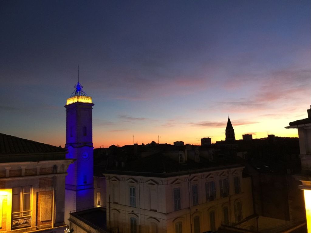Night view of Nîmes with the Clock Tower silhouetted against the sky
