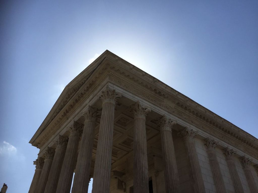 Low-angle view of the Maison Carrée Roman temple in Nîmes, France, Corinthian columns and ornate entablature seen against a bright midday sky