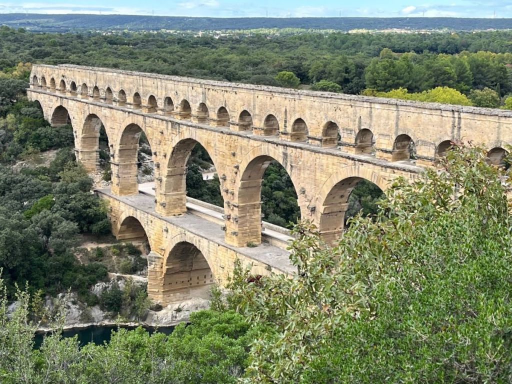 Aerial view of the Pont du Gard Roman aqueduct in southern France, three tiers of golden limestone arches rising above the Gardon river valley