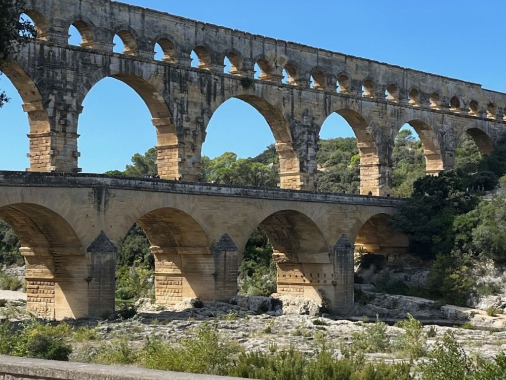 Close-up frontal view of the Pont du Gard aqueduct, showing the massive limestone piers and arches of the lower two tiers against a clear blue sky