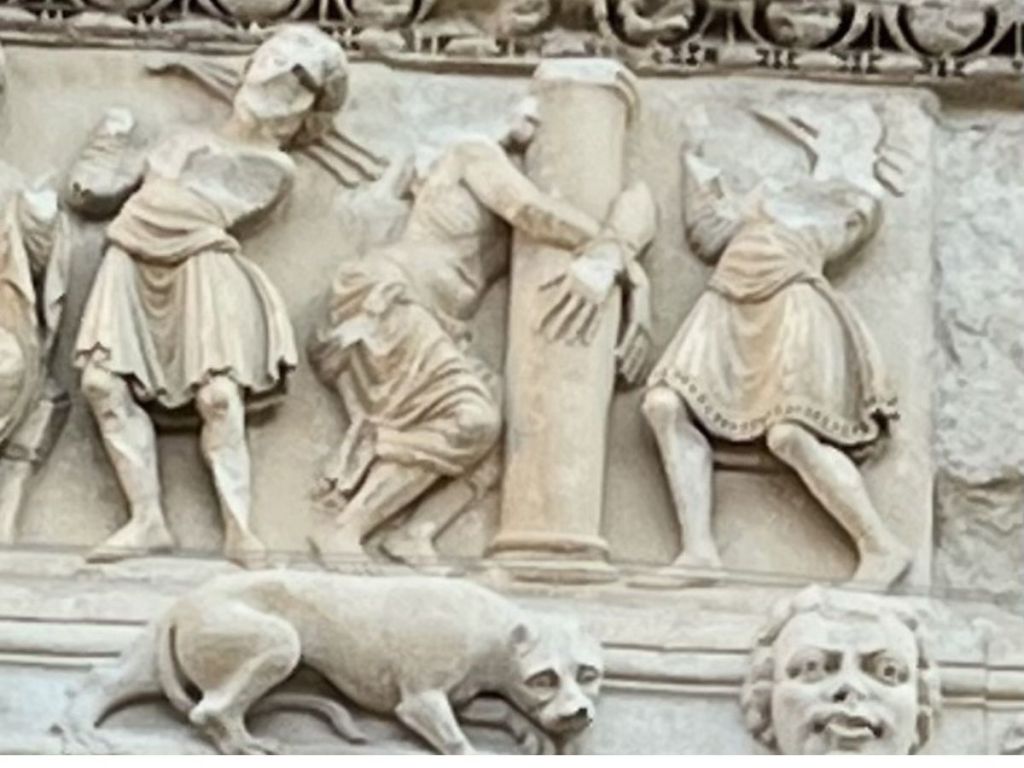 Detail of the Romanesque portal of Saint-Gilles Abbey in the Gard, France, showing intricately carved stone figures of medieval soldiers and a dog in low relief, circa 12th century