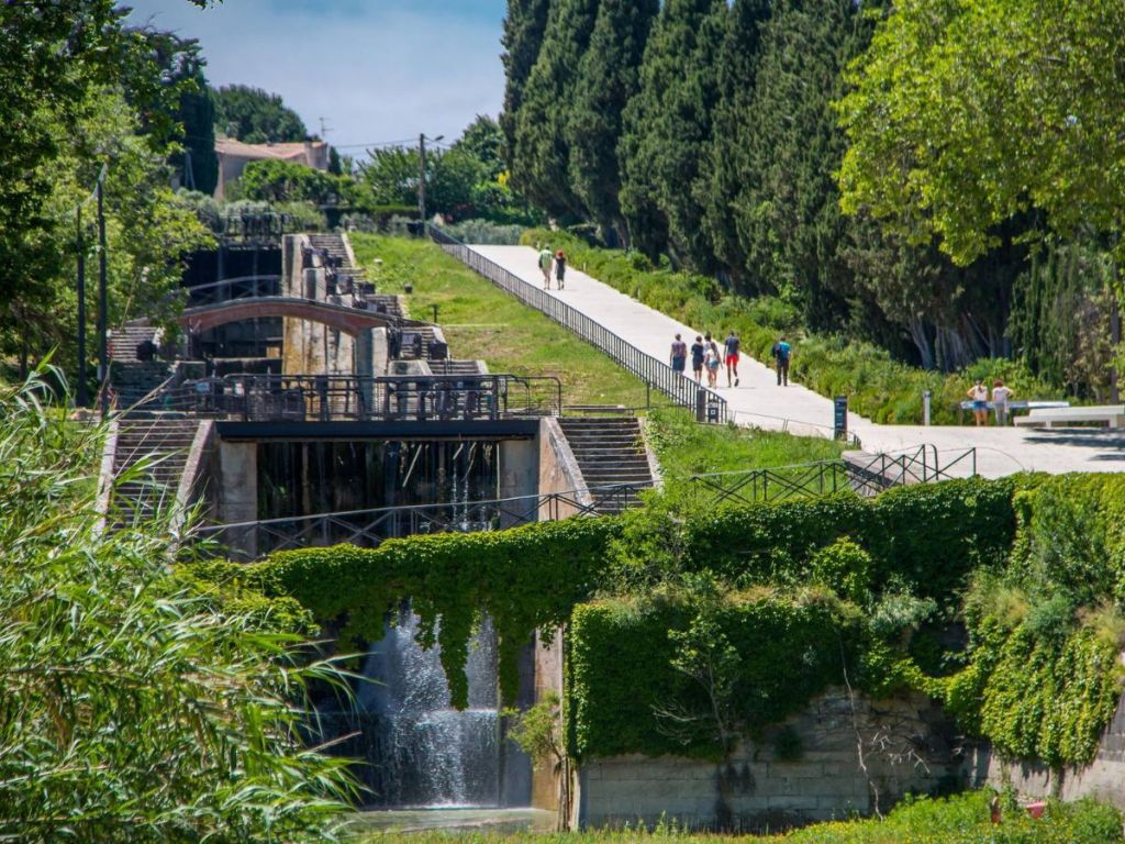 The staircase locks of Fonséranes on the Canal du Midi near Béziers, with cascading water, lush green vegetation and visitors strolling along the towpath in summer