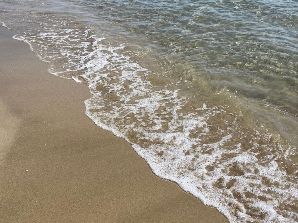 Gentle transparent waves washing over fine golden sand on a beach near Cap d'Agde, with crystal-clear Mediterranean water