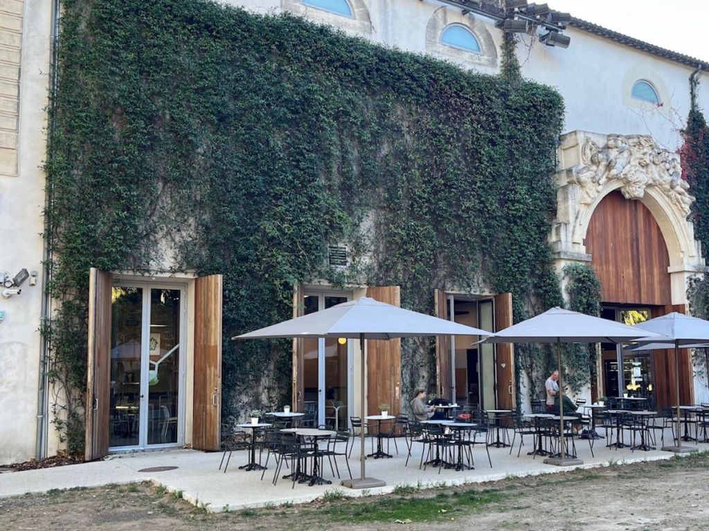 The entrance terrace of the Musée Fabre in Montpellier, with outdoor café tables under gray parasols set against an ivy-covered stone wall and a carved Baroque stone portal
