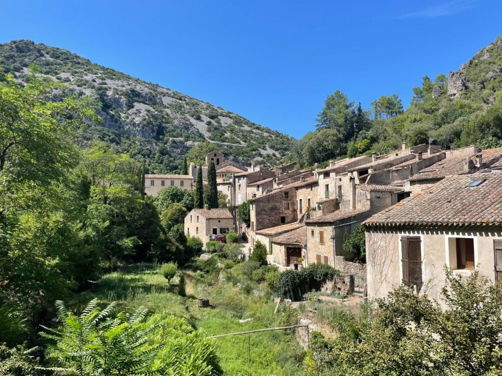 Panoramic view of Saint-Guilhem-le-Désert's medieval stone houses and terracotta rooftops nestled against a dramatic limestone mountain under a deep blue sky