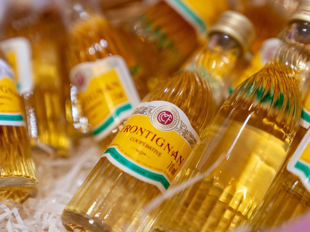 Close-up of small golden bottles of Muscat de Frontignan from the local cooperative, their amber color glowing against white packaging straw