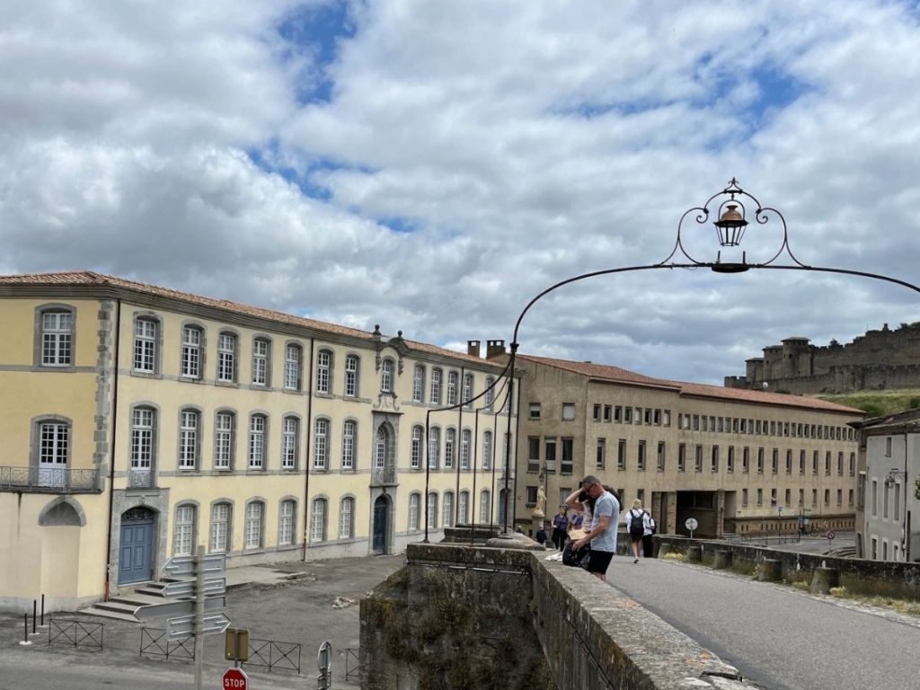 View of the Ancienne Manufacture Royale de Draps in Carcassonne's Bastide Saint-Louis, seen from the Pont Vieux, with the Cité in the distance