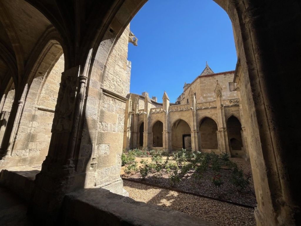 Gothic cloister galleries of Narbonne Cathedral surrounding a rose garden Caption: The 14th-century cloister, built on the site of the former Romanesque church, links the Archbishop's Palace with the Cathedral of Saints Just and Pastor.