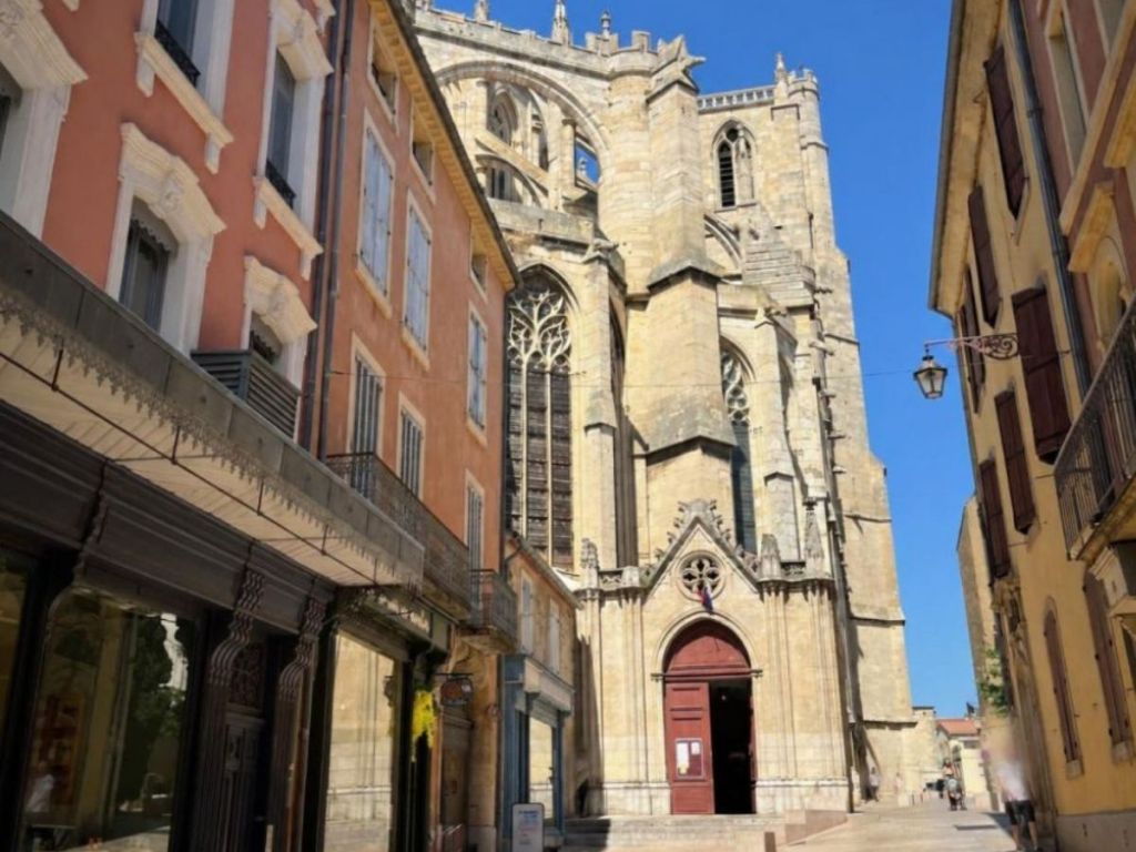 Gothic choir and flying buttresses of Narbonne Cathedral rising above a narrow street