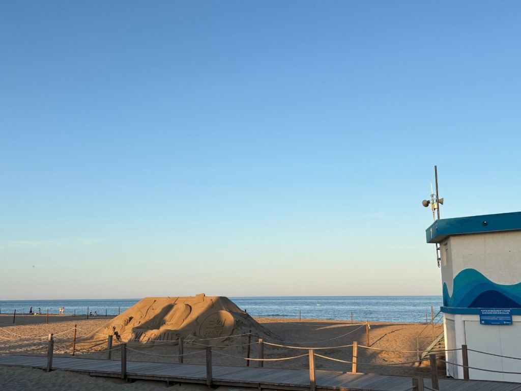 Sandy beach at Narbonne Plage at dusk, with a sand sculpture and a lifeguard post